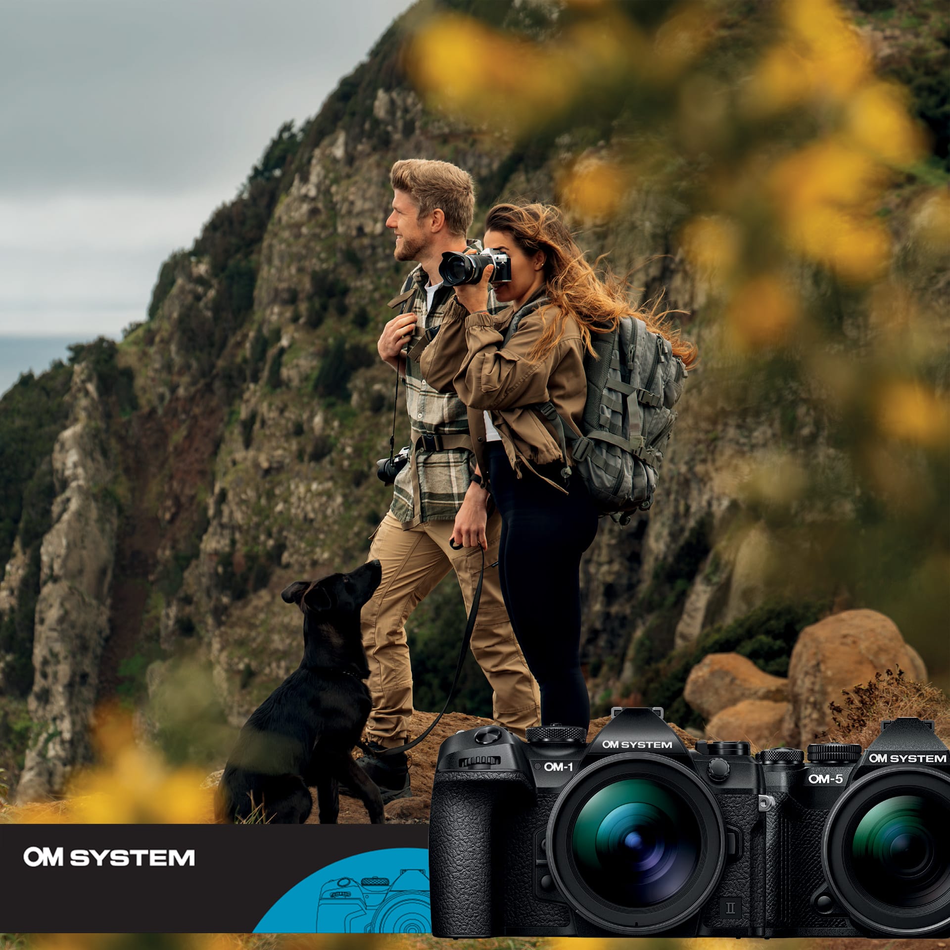 Two hikers with a black dog on a rocky cliff path, backpacks on, gazing toward the sea cliff scenery.